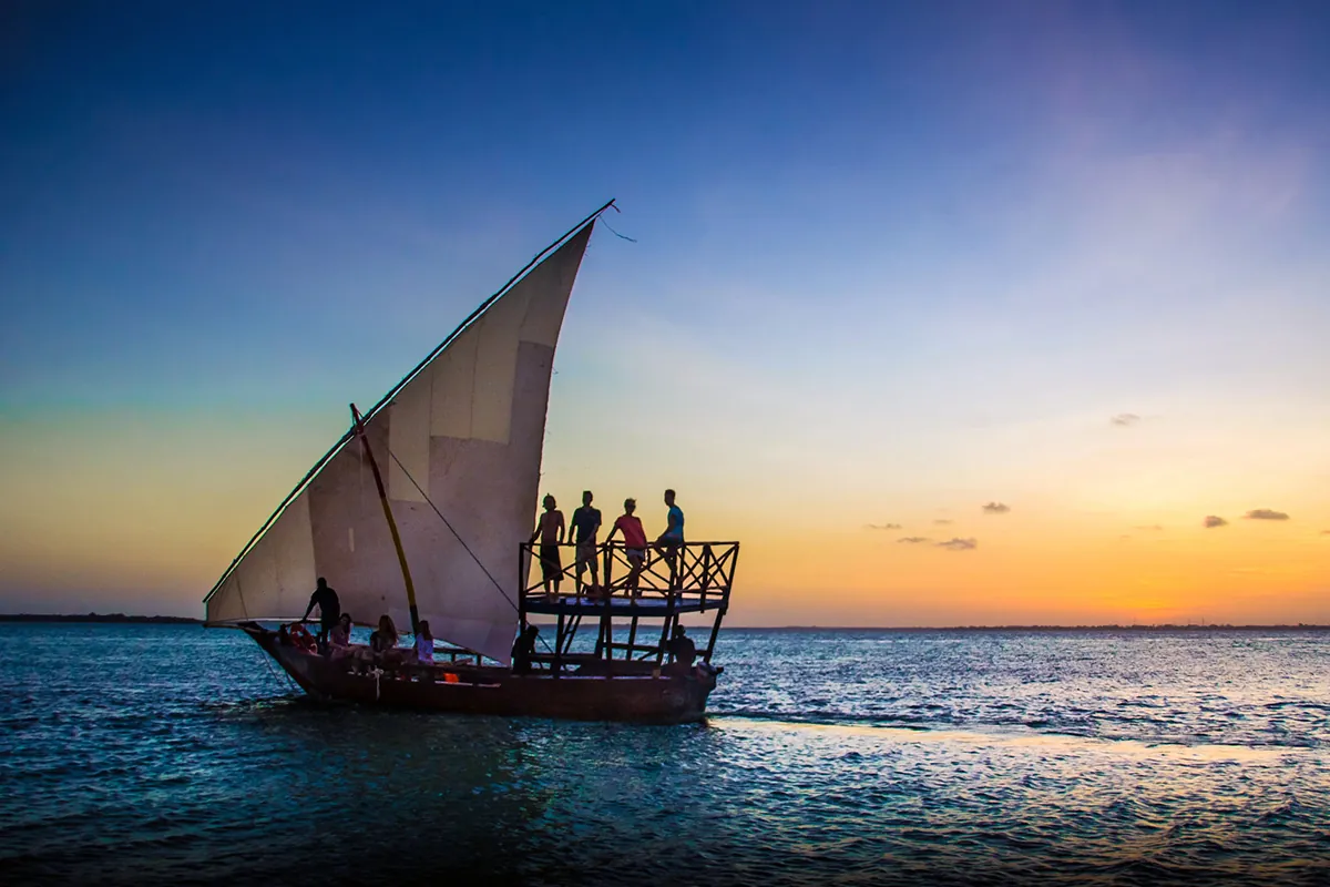 Guests standing on the deck of a dhow at sunset in Zanzibar